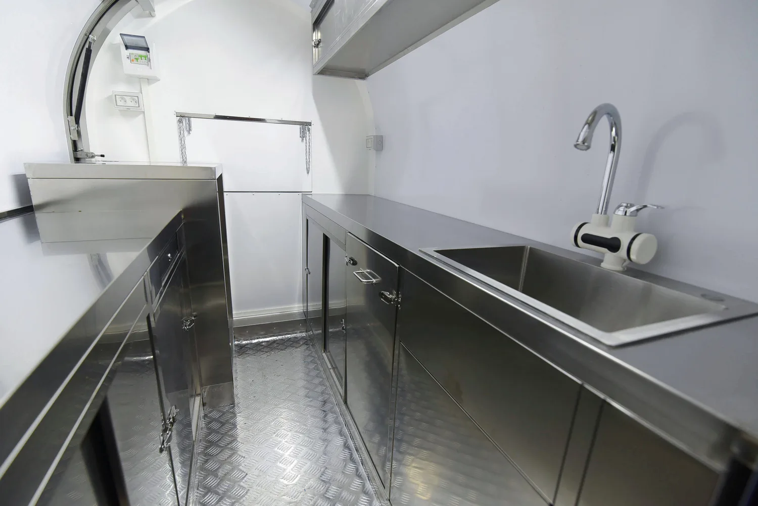 Intérieur d'une remorque : plans de travail et meubles en inox, évier avec eau chaude, sol aluminium antidérapant