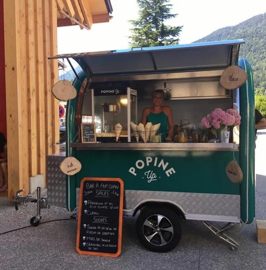 Remorque vert canard à l'enseigne Popine Up, machine à pop-corn et cornets prêts à servir sur le comptoir